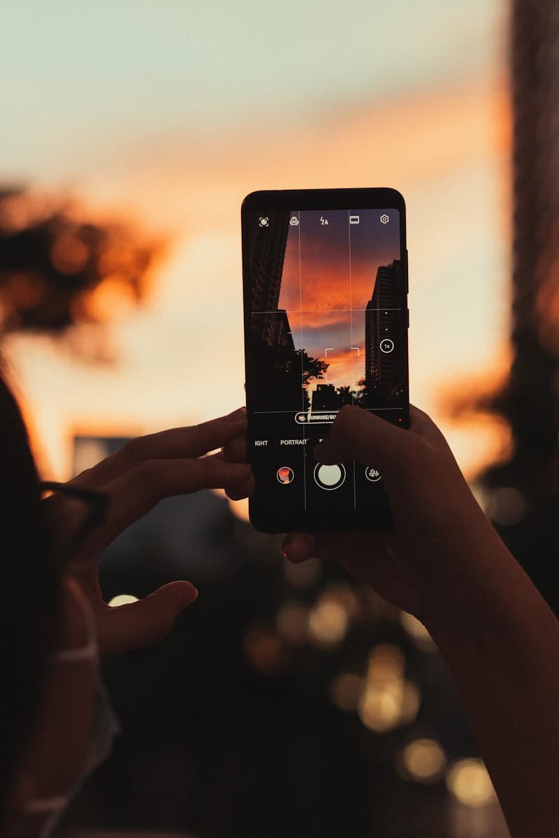 Gün batımında telefonla fotoğraf çeken bir kişinin eli (geçici görsel)